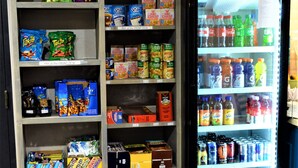 Una máquina expendedora llena de aperitivos y bebidas, junto a un estante con diversos productos envasados.
