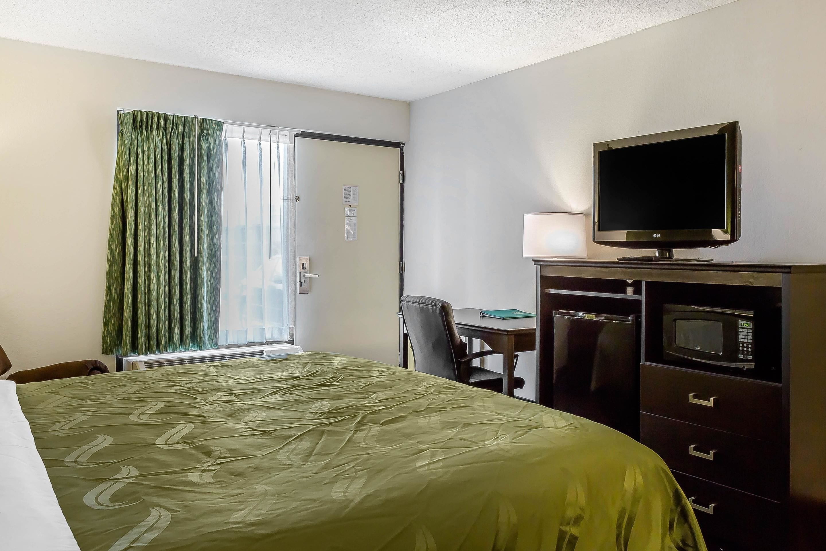Een hotelkamer met een bed, een bureau, een televisie en een magnetron.