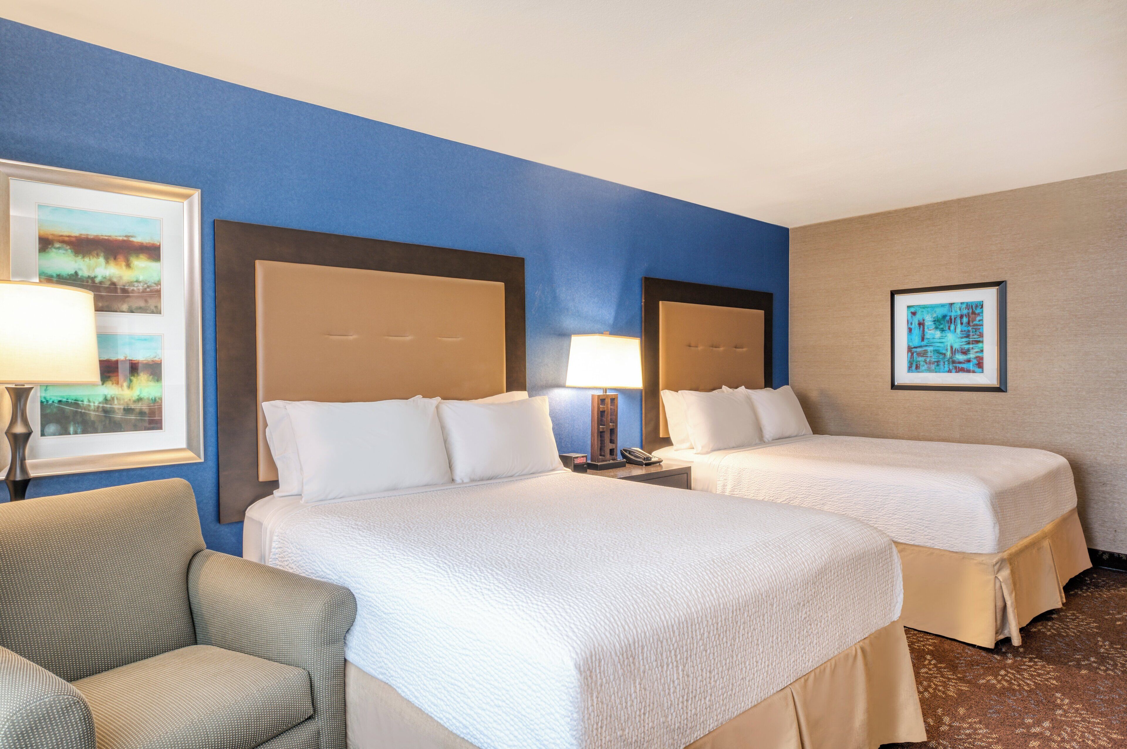 A hotel room with two beds, a chair, and artwork on the walls.