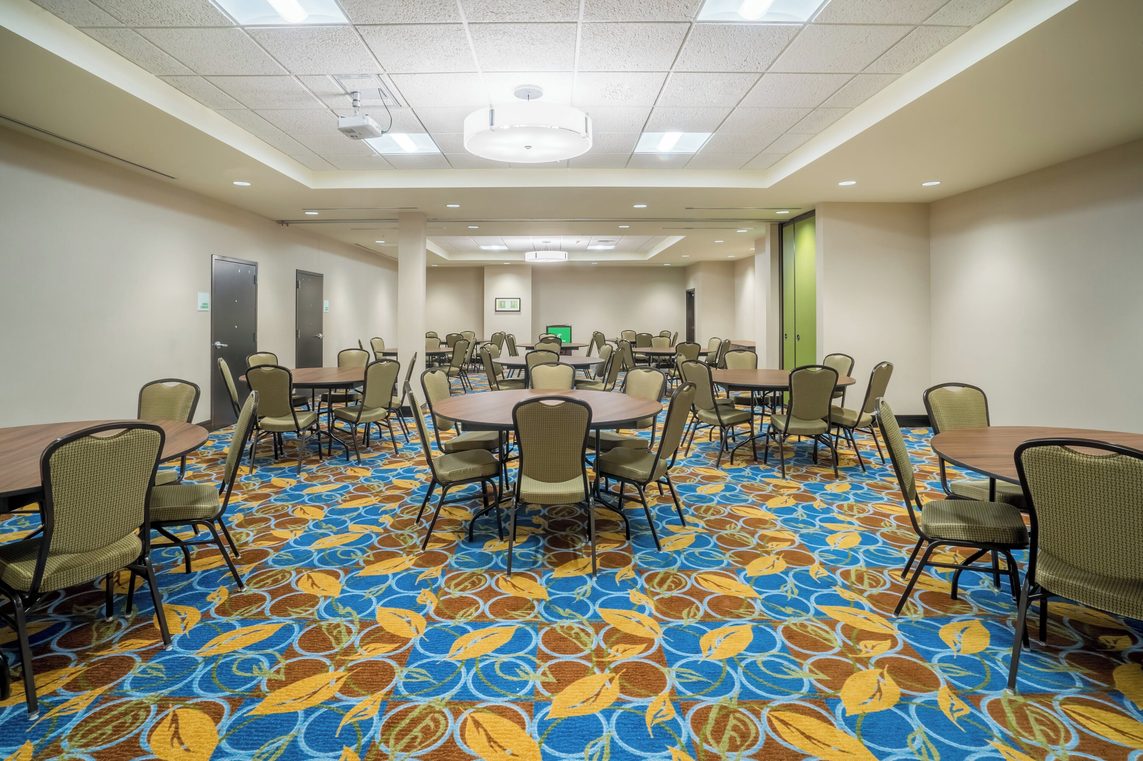 A conference room with multiple tables and chairs, a patterned carpet, and a ceiling with recessed lighting.