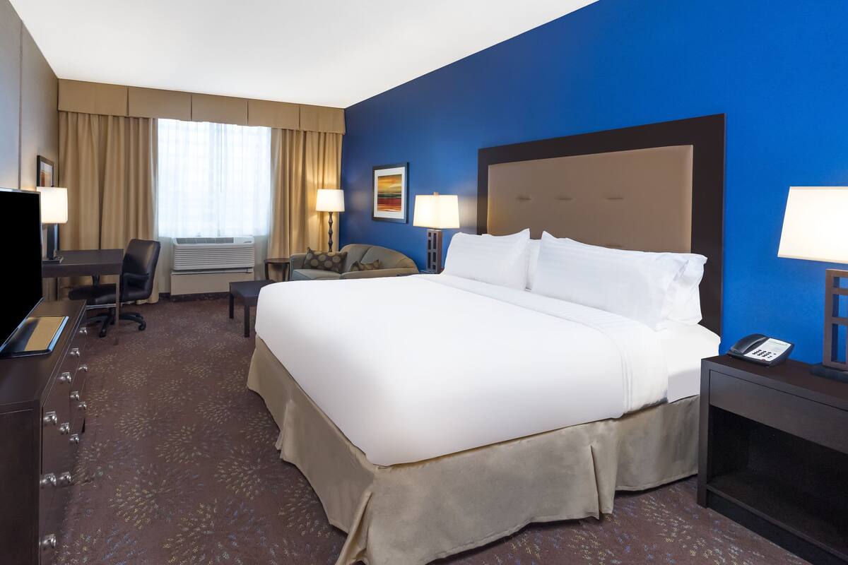 A hotel room with a large bed, a desk with a computer, a chair, and a TV.