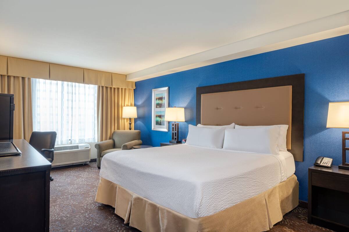 A hotel room with a large bed, a desk with a chair, a TV, and a lamp.