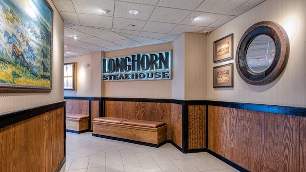 A reception area with a wooden bench, a wall-mounted sign for LongHorn Steakhouse, and a large painting. - Holiday Inn Terre Haute by IHG (Terre Haute)