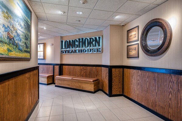 Un espace d’accueil avec un banc en bois, une enseigne murale pour le restaurant LongHorn Steakhouse et un grand tableau.