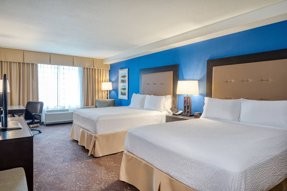 A hotel room with two beds, a desk, a chair, and a TV.