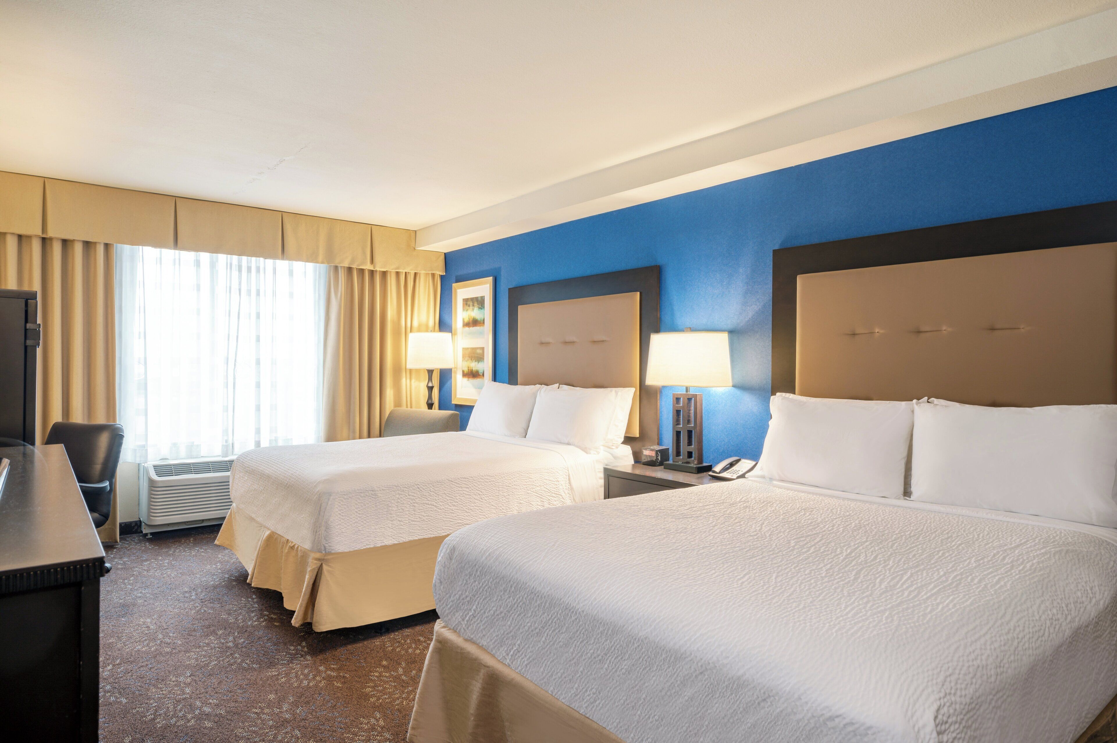 A hotel room with two beds, a desk, and a chair.