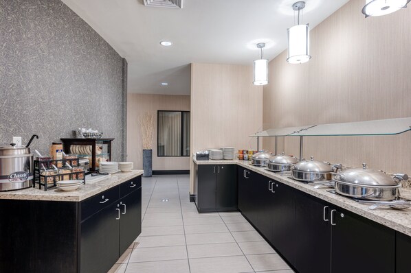 A modern kitchen with a granite countertop, black cabinets, and stainless steel appliances. There are multiple serving stations with food containers and utensils. - Holiday Inn Terre Haute by IHG (Terre Haute)