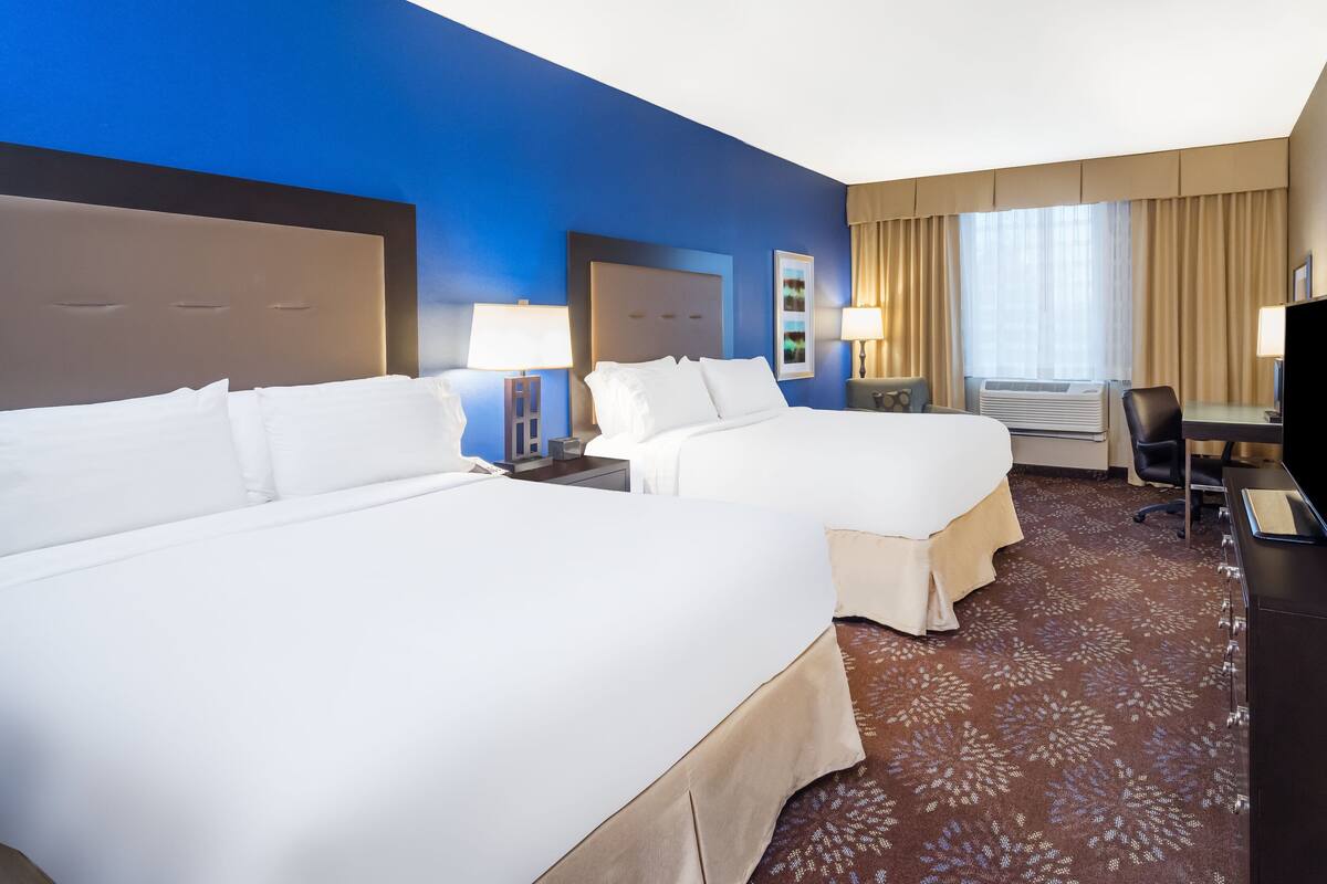 A hotel room with two beds, a desk, a chair, and a TV.
