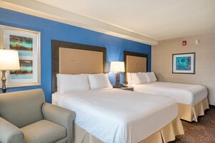 A hotel room with two beds, a chair, and artwork on the walls.
