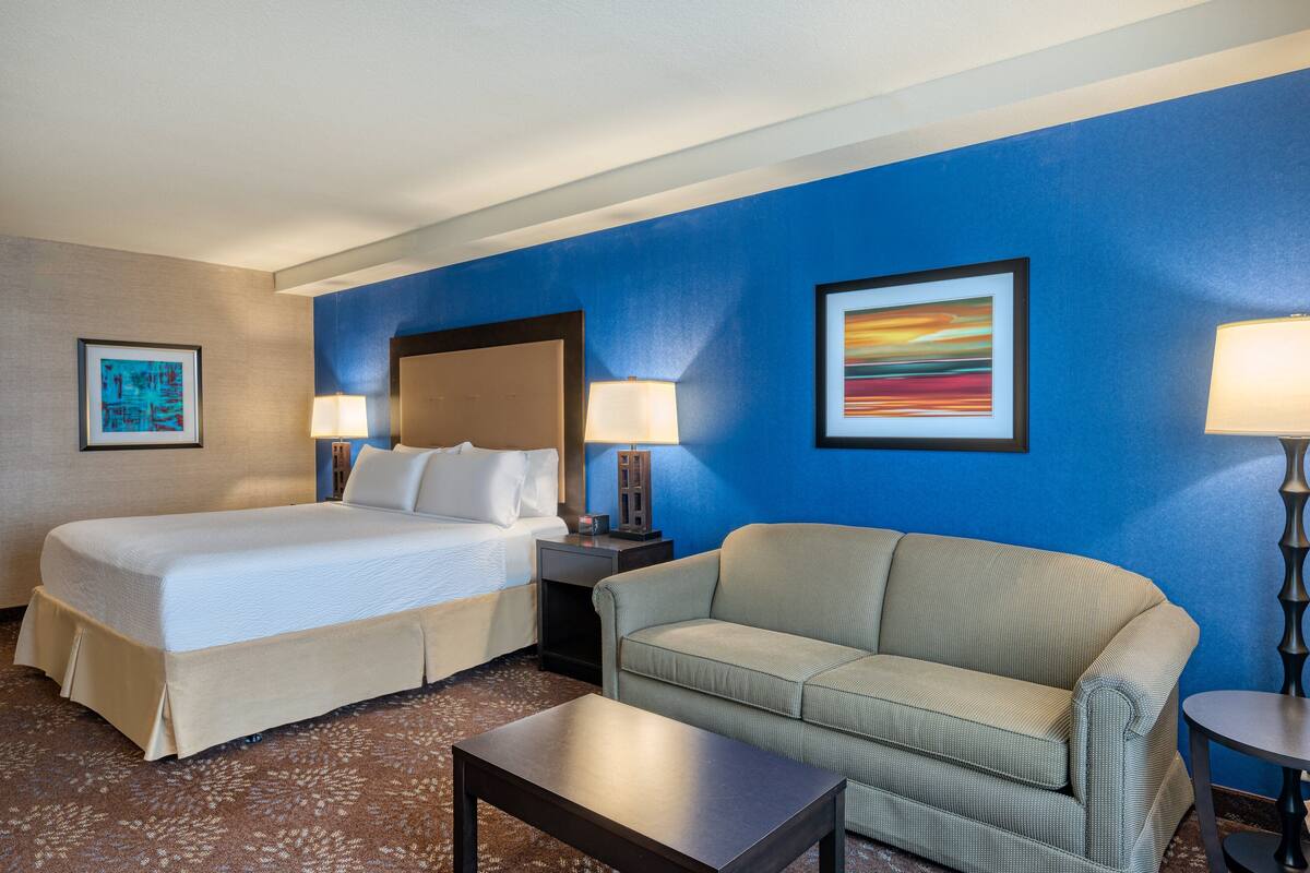 A hotel room with a bed, a sofa, a coffee table, and two lamps.