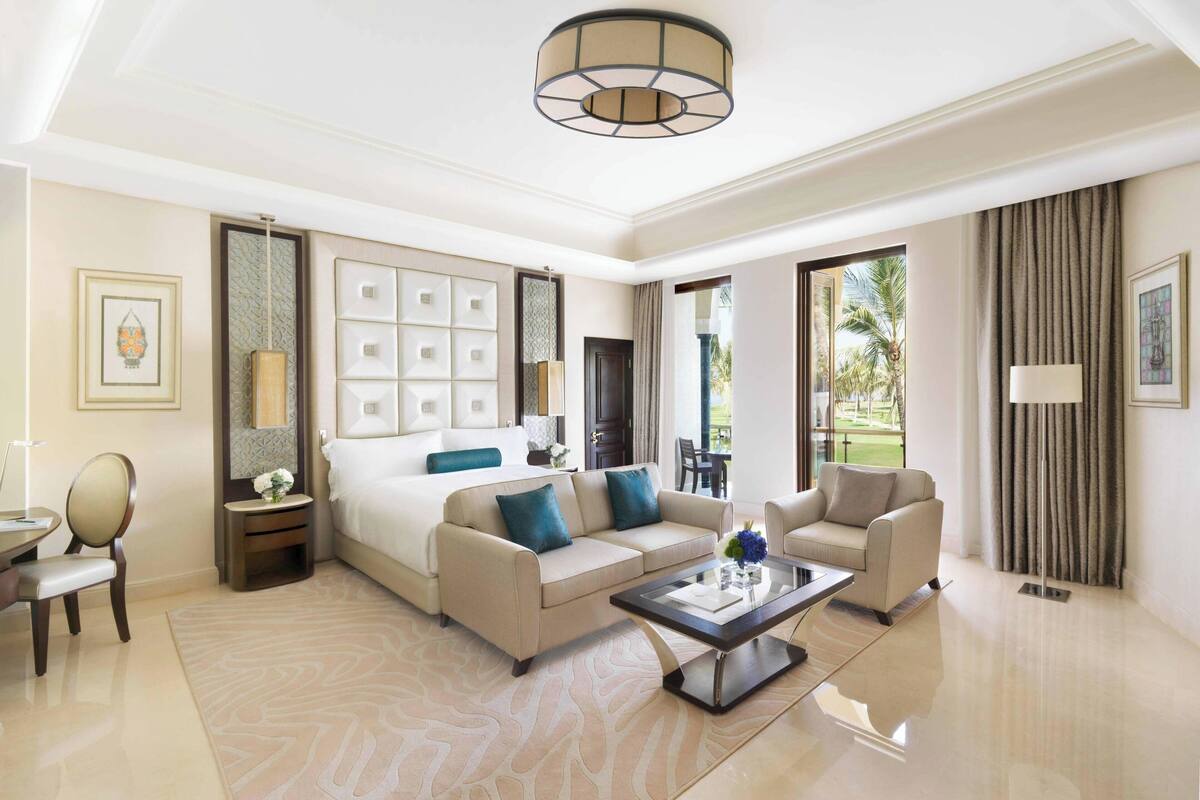 A spacious hotel room with a large bed, a sofa, a coffee table, and a view of the outdoors.
