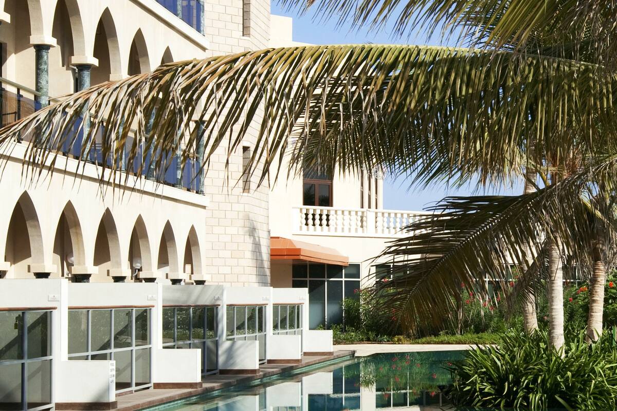 A pool with clear water reflecting the building and palm trees.