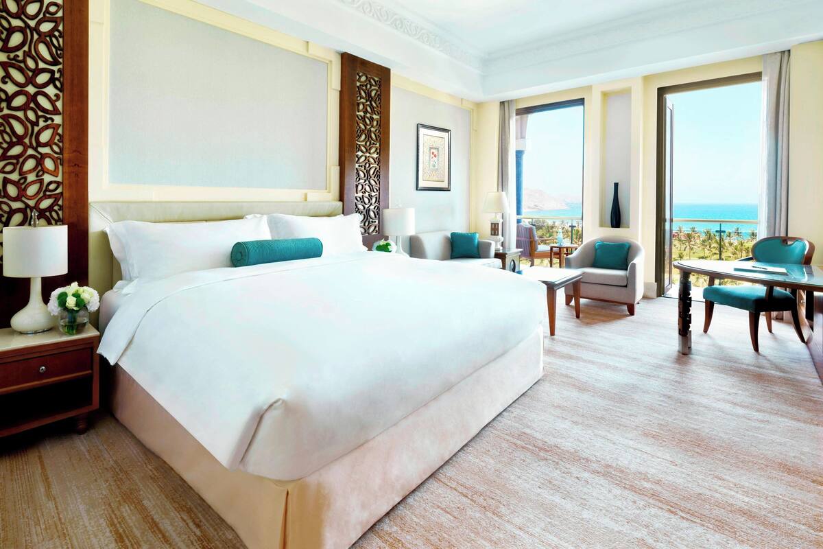 A hotel room with a large bed, a sitting area with a table and chairs, and a balcony with a view.