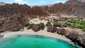 A coastal resort with a white building surrounded by rocky terrain and a turquoise beach.
