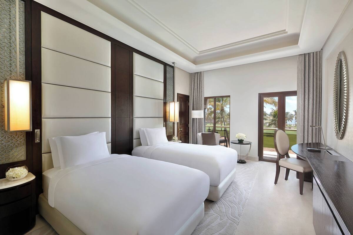 A hotel room with two beds, a desk, and a view of the outdoors.