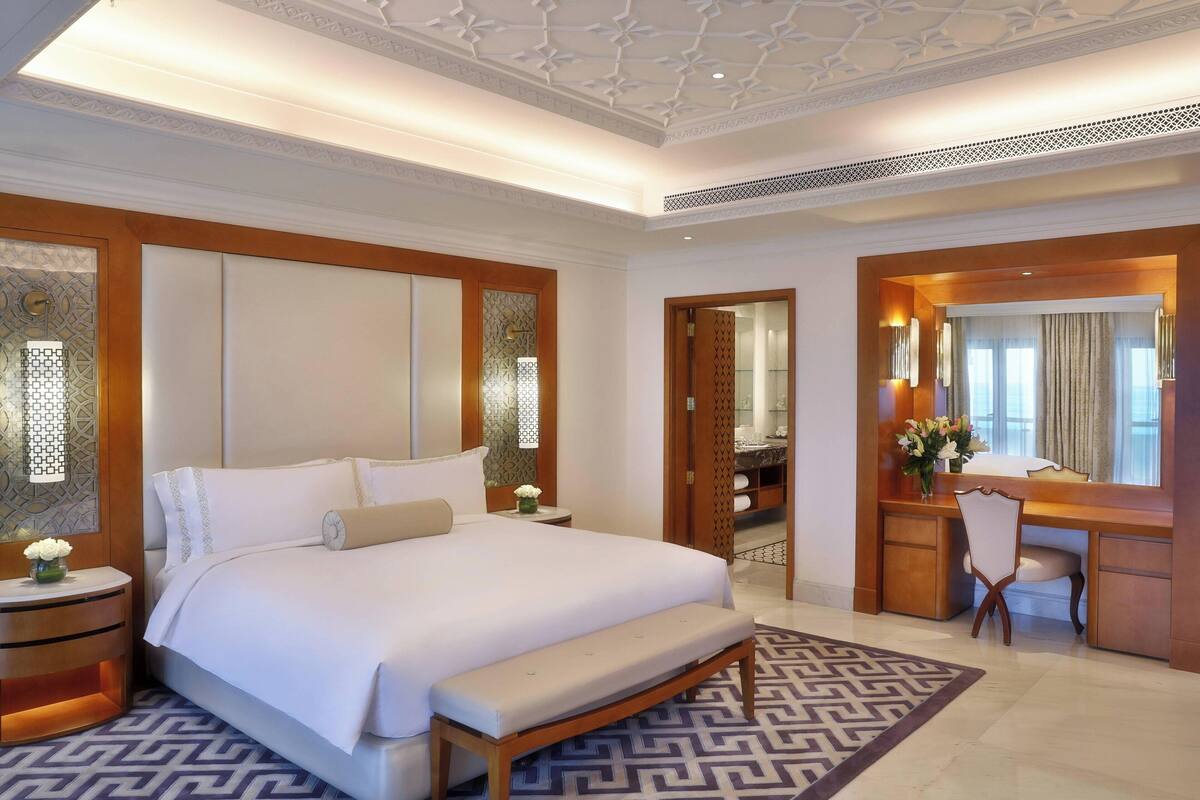 A spacious bedroom with a large bed, a wooden desk, and a vanity with a mirror.