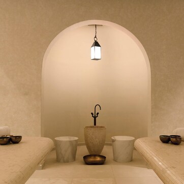 A spa room with two beds, a central stone basin, and a hanging light fixture.
