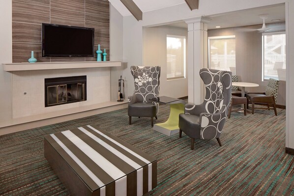 A modern hotel room with a flat-screen TV mounted above a fireplace, two patterned armchairs, a striped ottoman, and a dining area with a round table and chairs. - Residence Inn by Marriott Ontario Airport (Ontario)