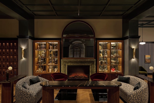 A room with a fireplace, two armchairs, a dining table, and a bookshelf. - Dearborn Inn, Autograph Collection (Dearborn)