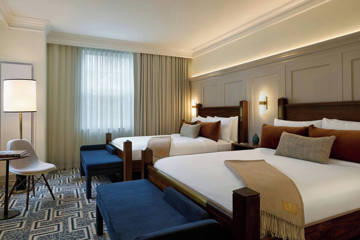 A hotel room with two beds, a desk, a chair, and a large window with curtains.