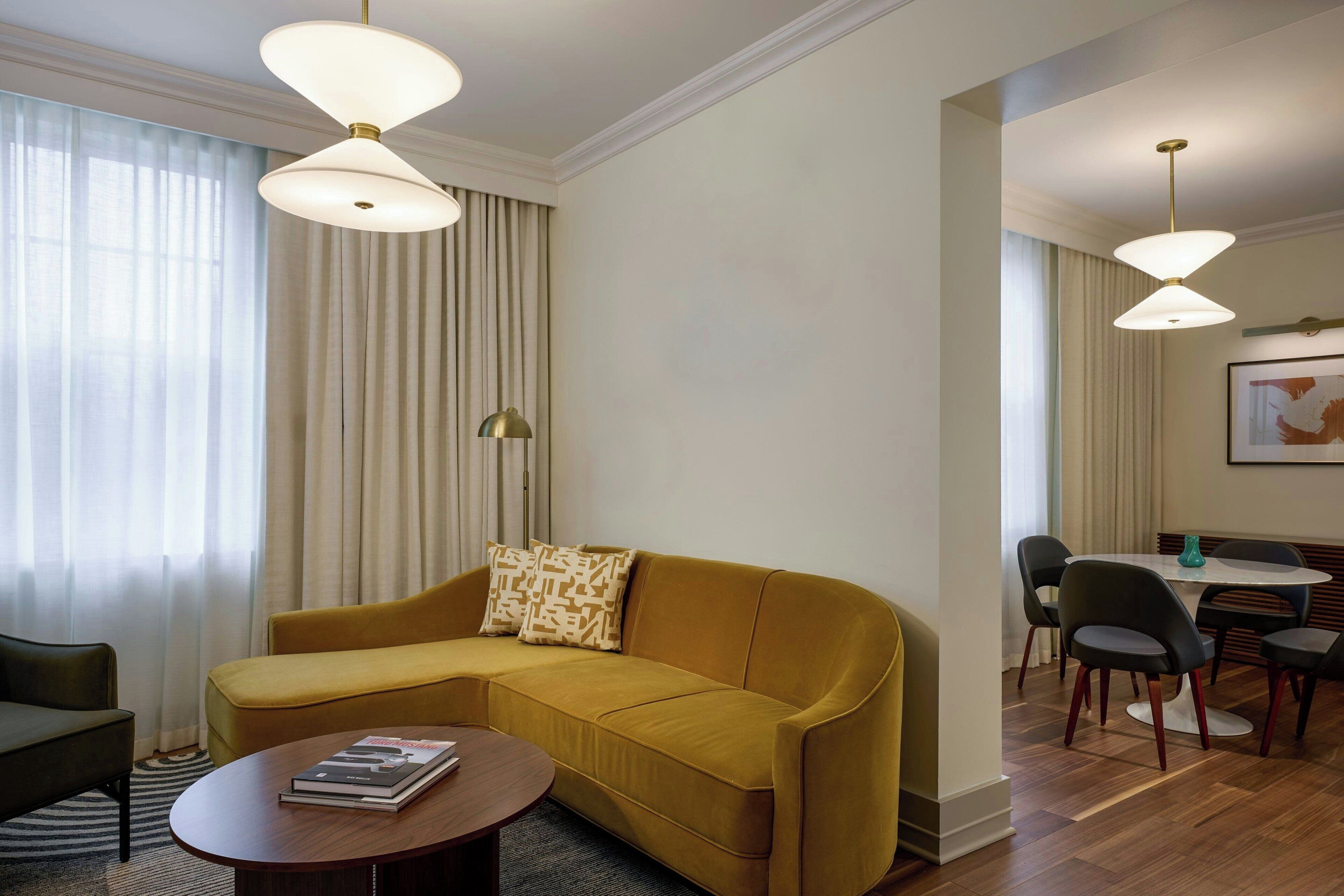 A modern living room with a mustard sofa, a round coffee table, and a dining area with a table and chairs.