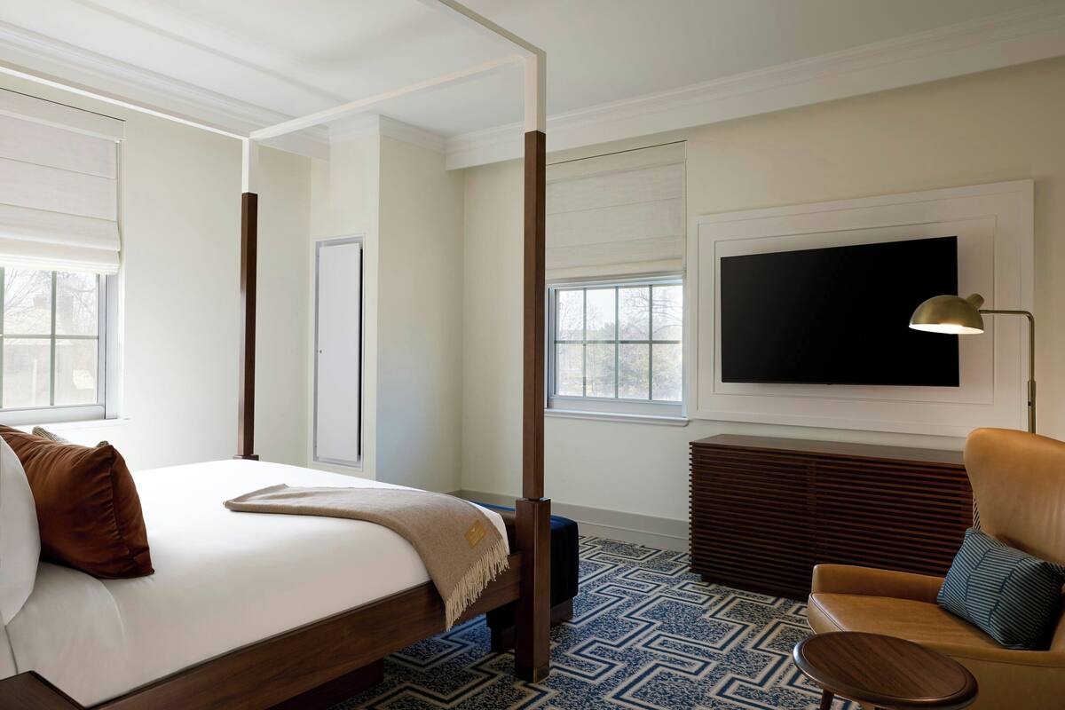 A hotel room with a four-poster bed, a television mounted on the wall, a sofa, and a patterned floor.