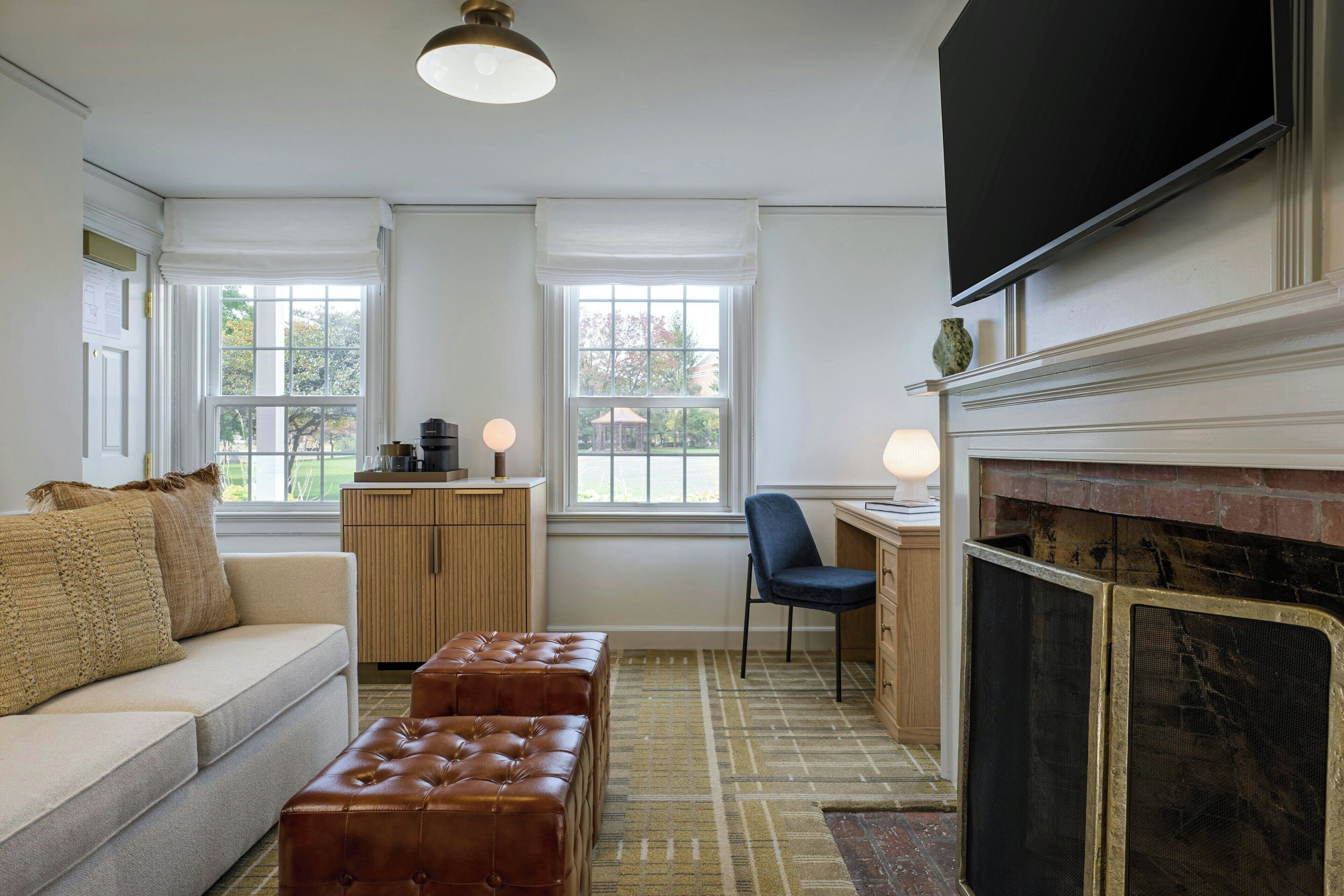 A living room with a sofa, ottoman, fireplace, television, and windows.