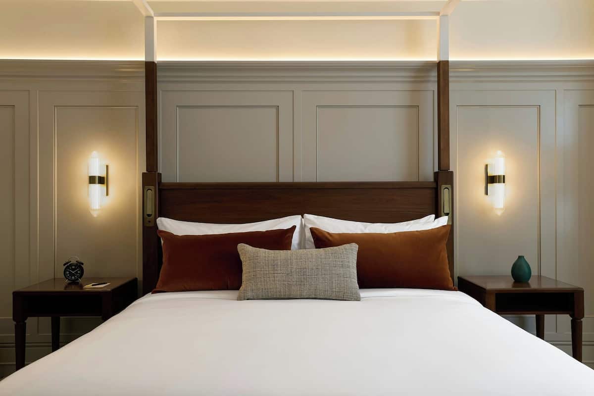 A neatly made bed with a wooden headboard, two bedside tables, and wall-mounted lights.