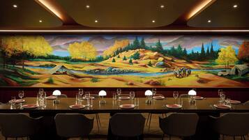 Un espace repas agrémenté d’une fresque représentant un paysage, une longue table dressée pour un repas et plusieurs chaises.