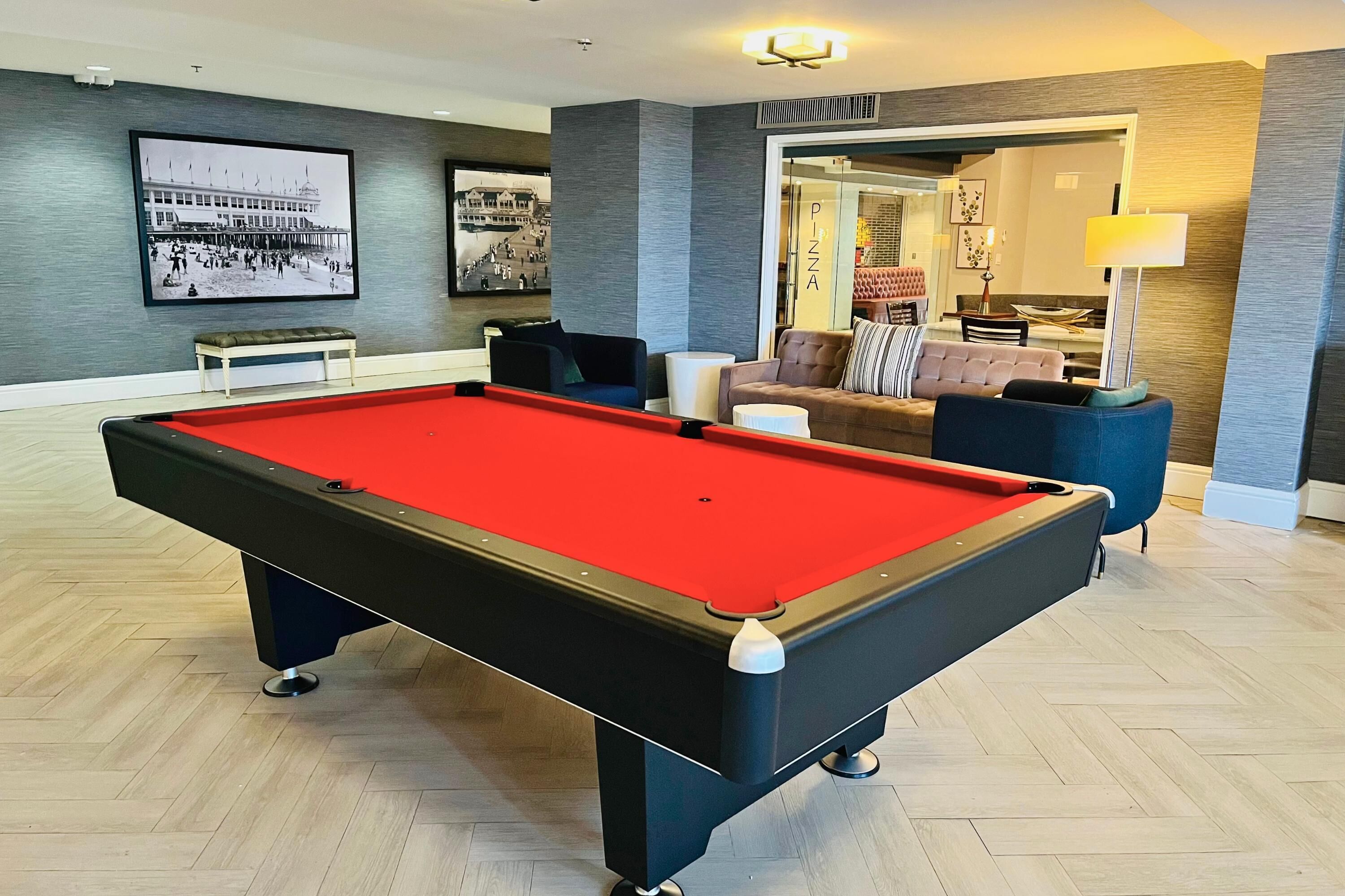 A pool table in a room with a herringbone floor pattern, a sofa, and a lamp.