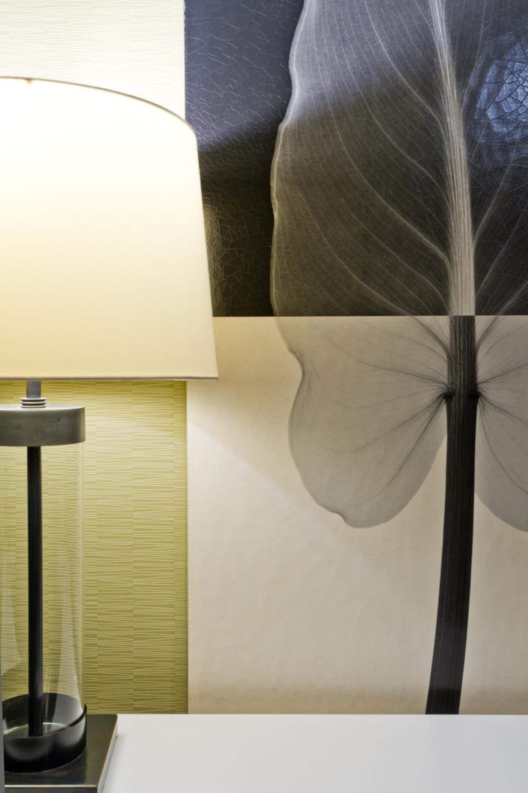En lampa står på ett bord framför en vägg som har ett stort bladmotiv.