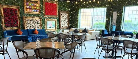A restaurant with a green wall decorated with framed pictures, a blue sofa, and wicker chairs.