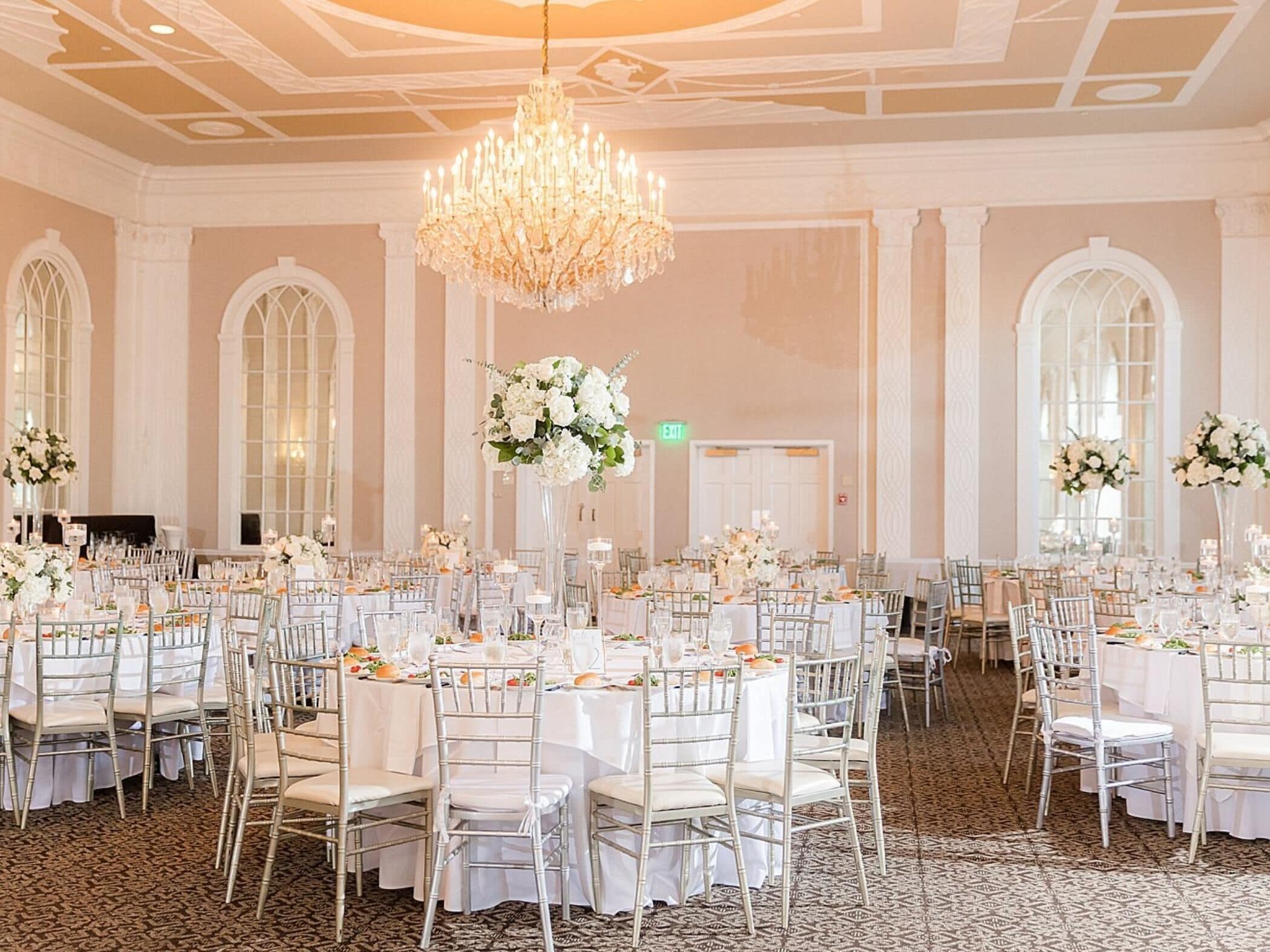 A banquet hall with round tables, white chairs, and floral centerpieces.