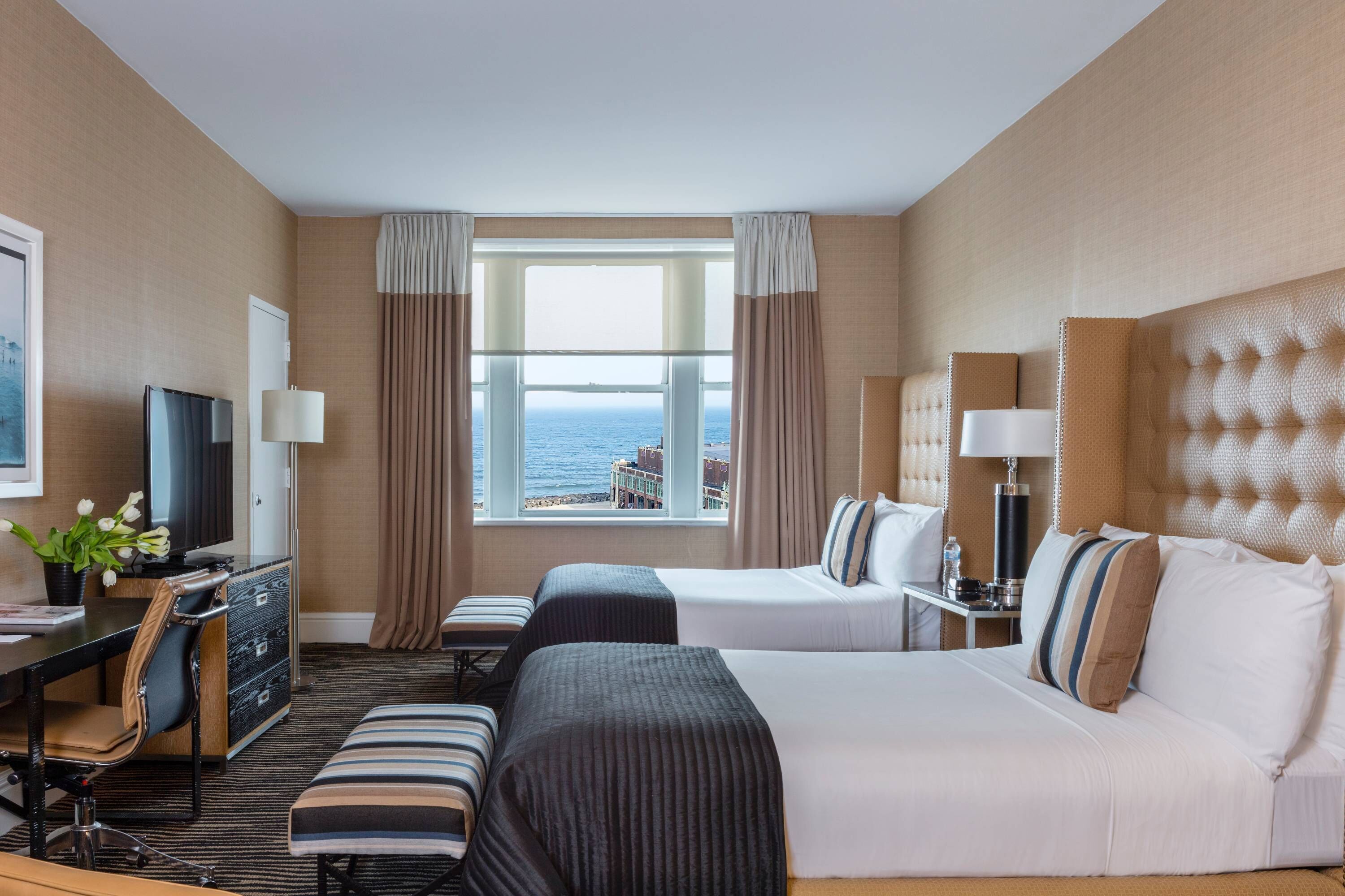 Une chambre d’hôtel avec deux lits, un bureau, une chaise, une télévision et une vue sur la mer.