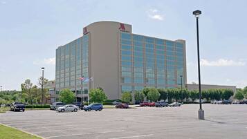 A large, modern hotel with a curved facade, multiple floors, and a parking lot in front.