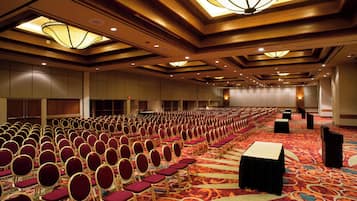 Un salón de conferencias con filas de sillas, un escenario y suelo alfombrado.