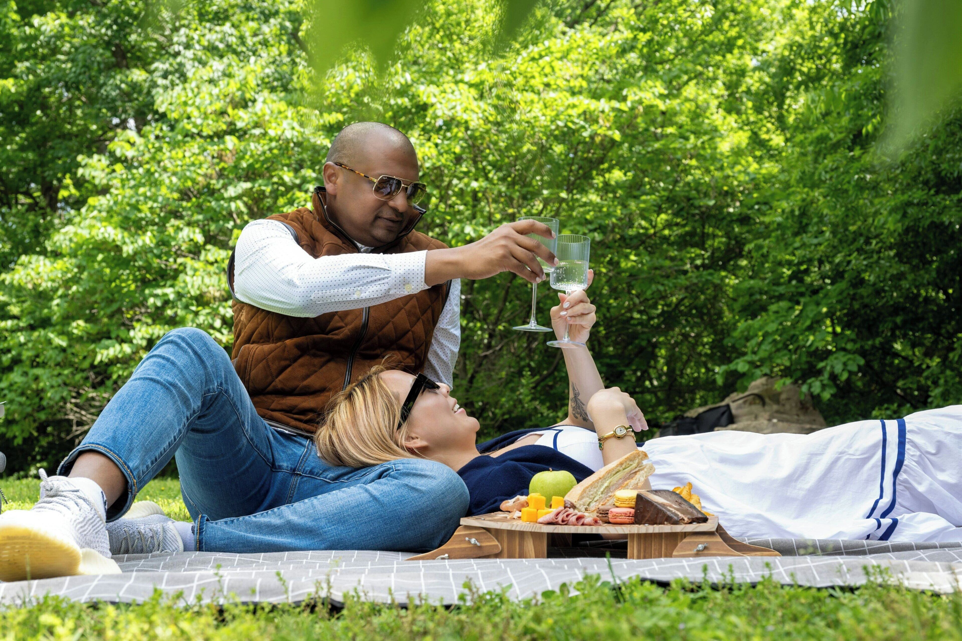 Una pareja descansando al aire libre sobre una manta de picnic, con comida y bebidas.