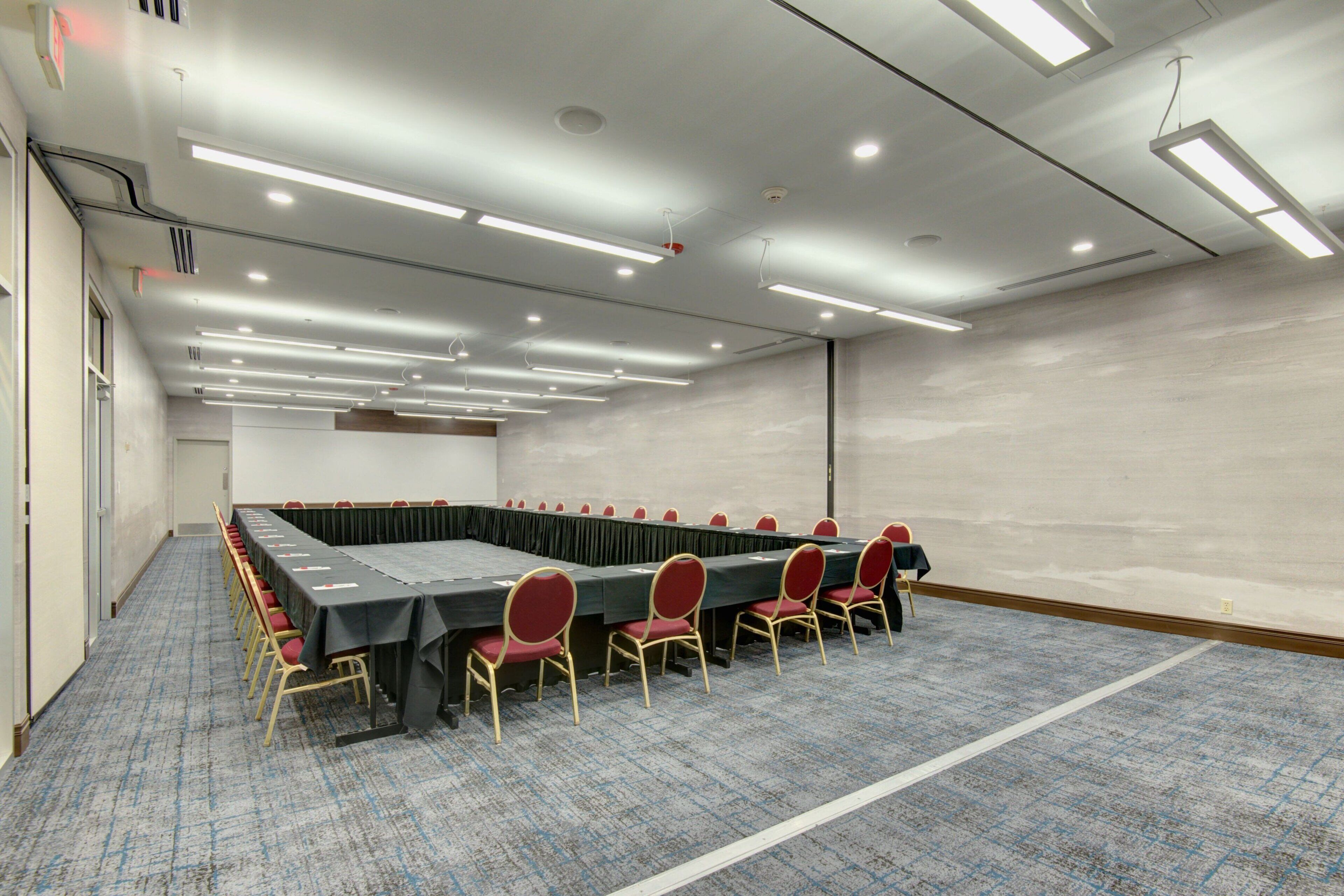 A conference room with a long table, red chairs, and carpeted flooring.
