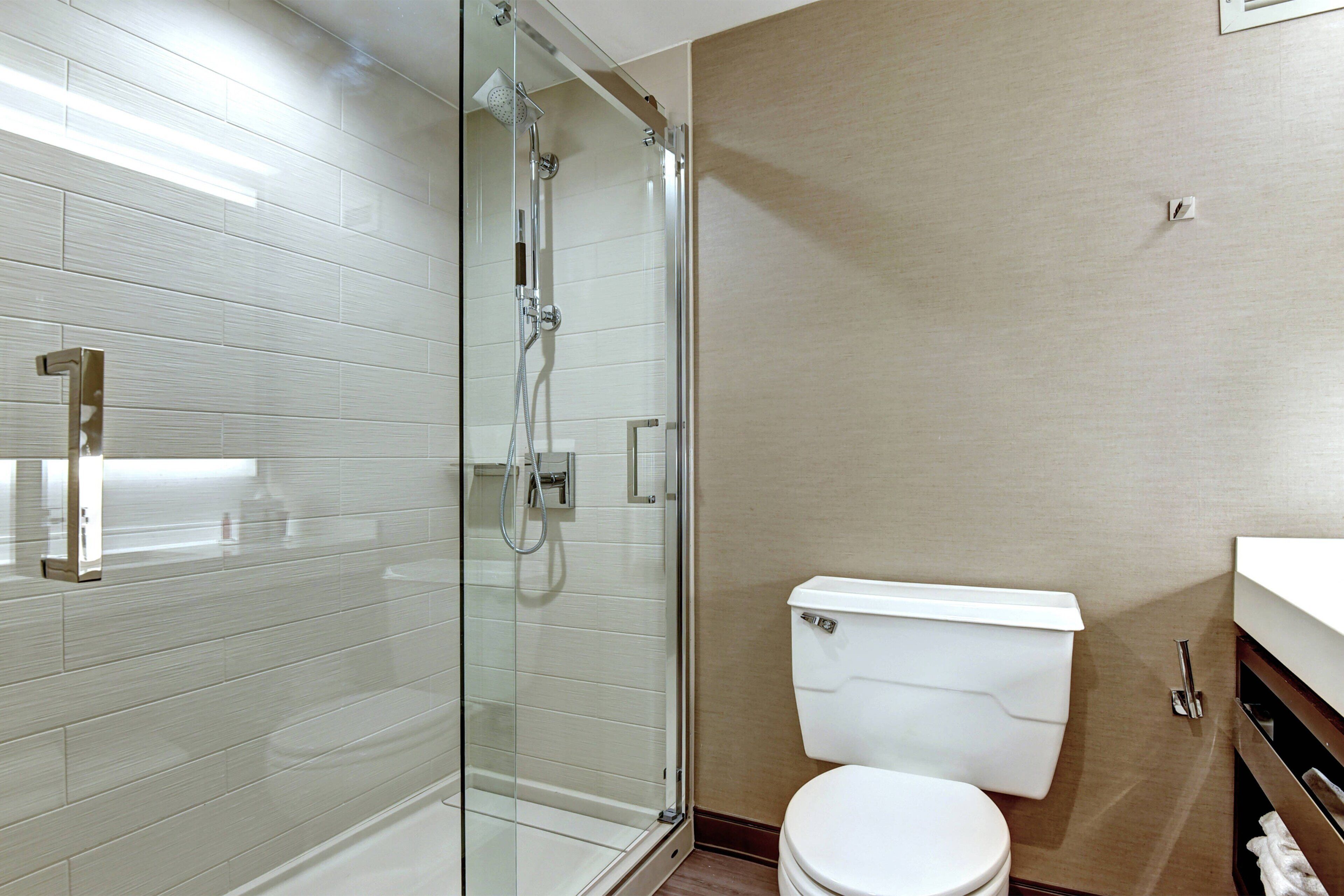 A modern bathroom with a glass-enclosed shower, a white toilet, and a wooden vanity.