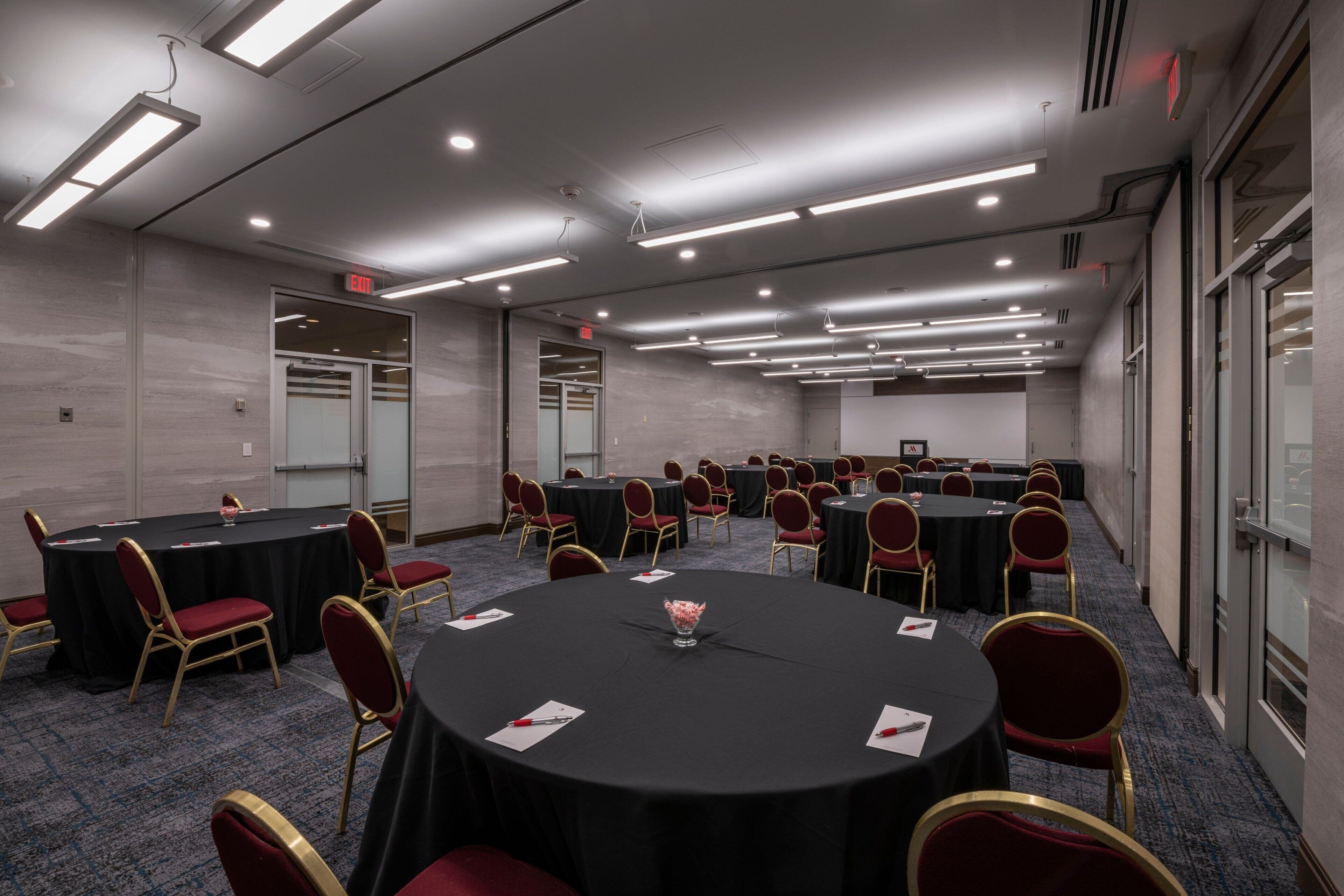 Un salón de conferencias con varias mesas redondas, cada una con mantel negro y sillas rojas.