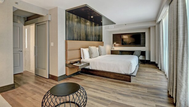 A modern hotel room with a large bed, a TV, a small table, and a unique ceiling design. - Marriott Tulsa Hotel Southern Hills (Tulsa)