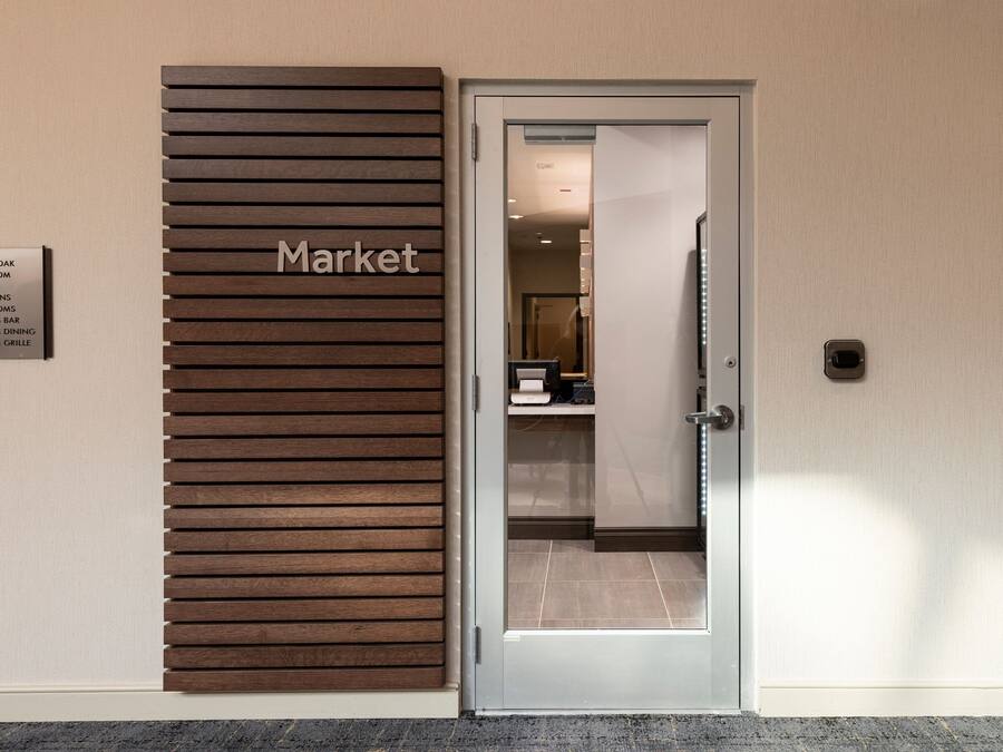 Entrada de hotel con un panel de madera que dice 'Market' y una lista de servicios que incluye un roble centenario, salón de baile, ascensores, baños y un bar con césped alto.