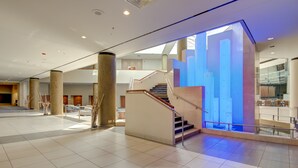 A spacious lobby with a central staircase, large pillars, and a modern glass wall. - Marriott Tulsa Hotel Southern Hills (Tulsa)
