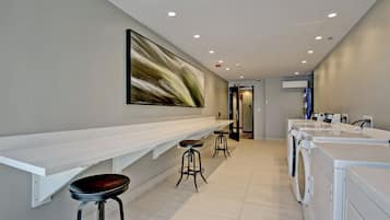 A modern laundry facility with a long counter, two stools, and multiple washing machines.