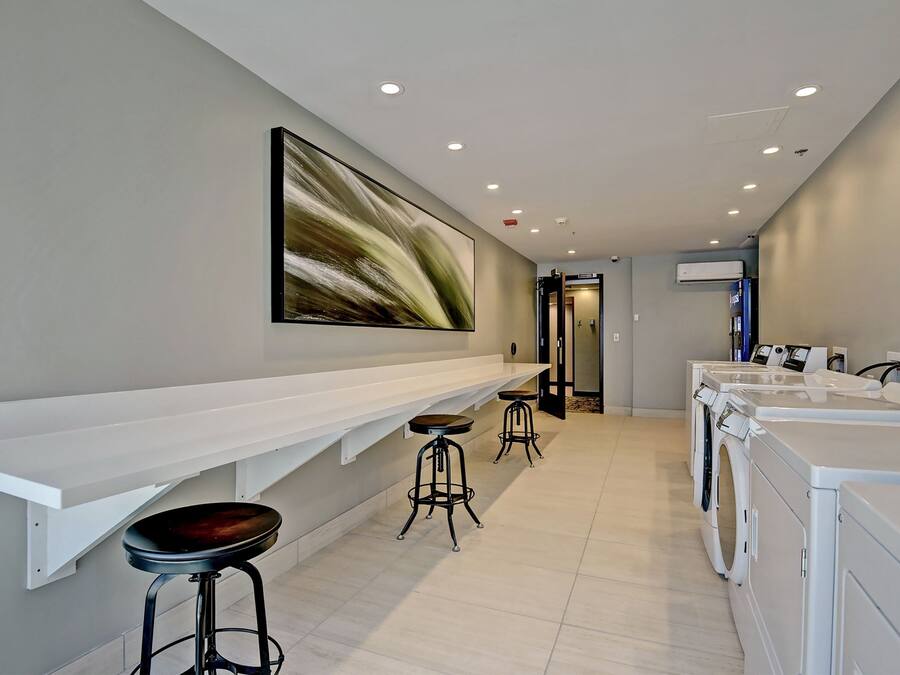 A modern laundry facility with a long counter, two stools, and multiple washing machines.