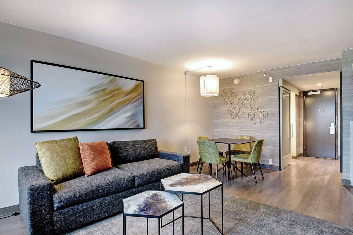 A modern living room with a grey sofa, two side tables, and a dining area with a table and chairs.