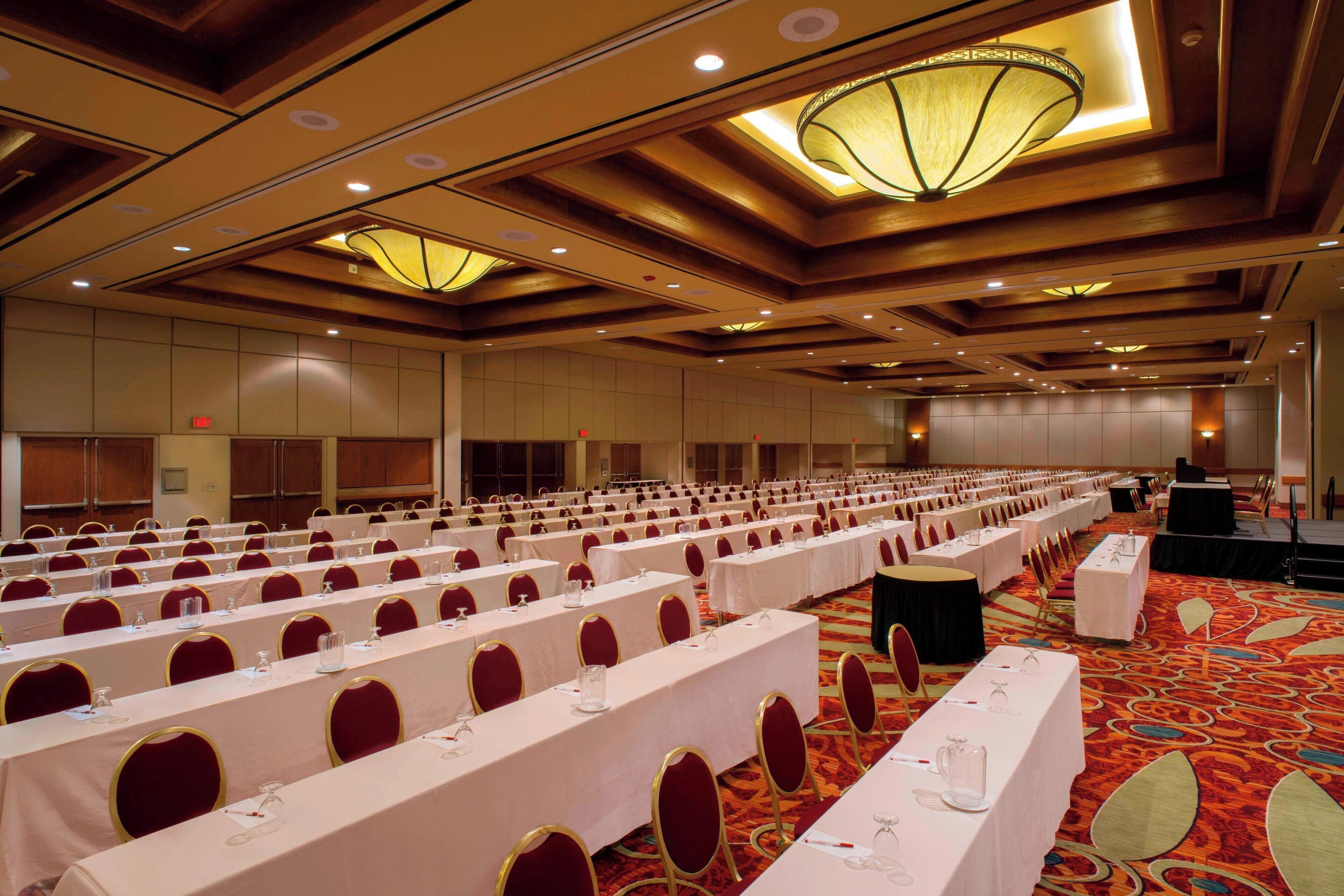 A large conference room with rows of tables and chairs, a stage, and a carpeted floor.