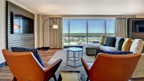 A modern living room with a large window, a sofa, two armchairs, a small table, and a TV mounted on the wall. - Marriott Tulsa Hotel Southern Hills (Tulsa)