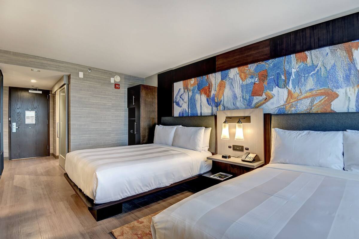 A hotel room with two beds, a large abstract painting on the wall, and a modern design.