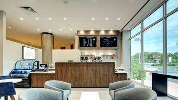 A modern reception area with a wooden counter, two grey armchairs, a coffee machine, and a large window offering a view of the parking lot.
